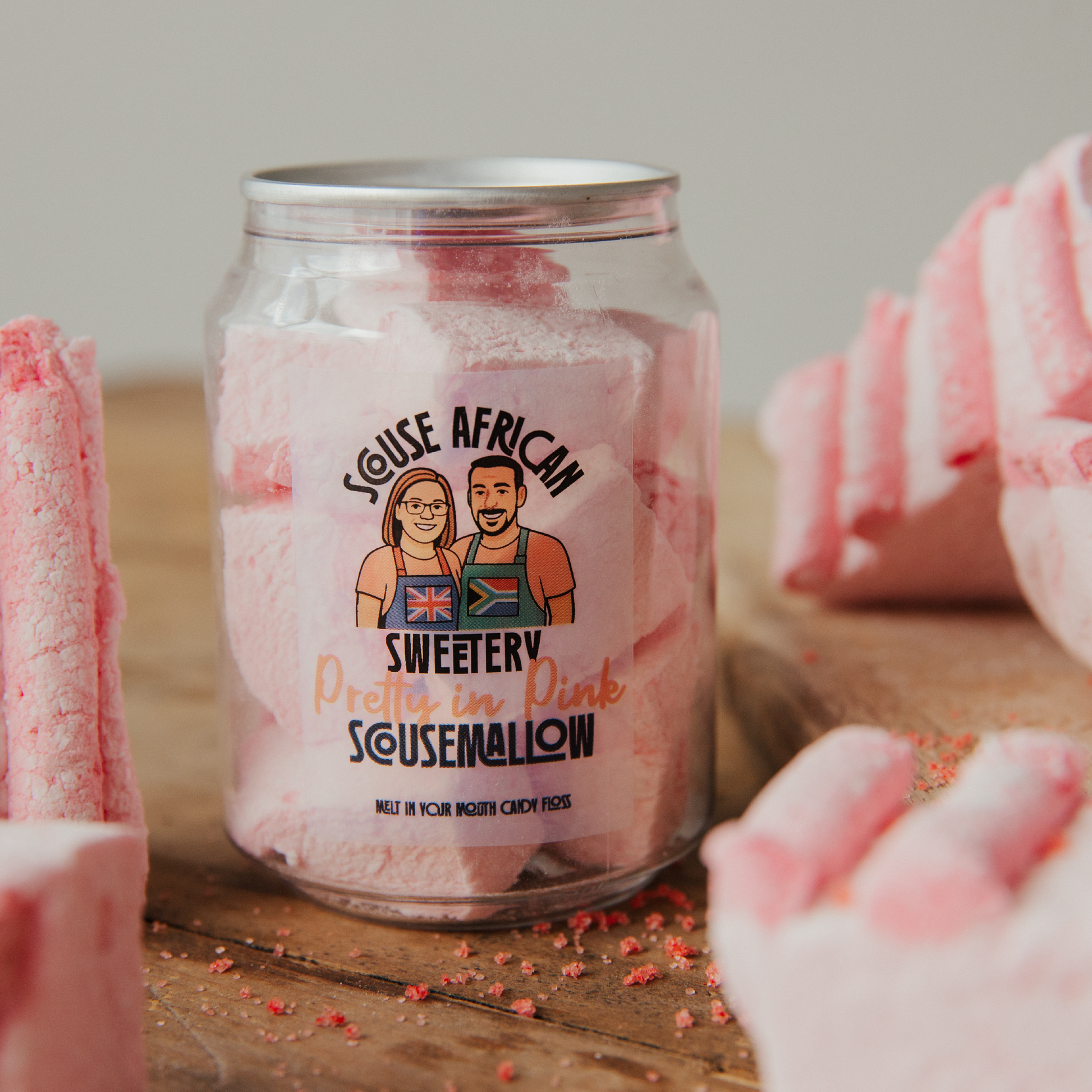 Jar of pink marshmallows with a label featuring two people and text on a wooden surface.