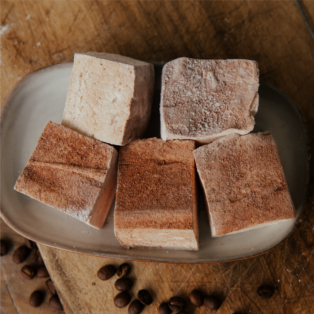 Chocolate coated marshmallows on a plate with coffee beans on a wooden surface