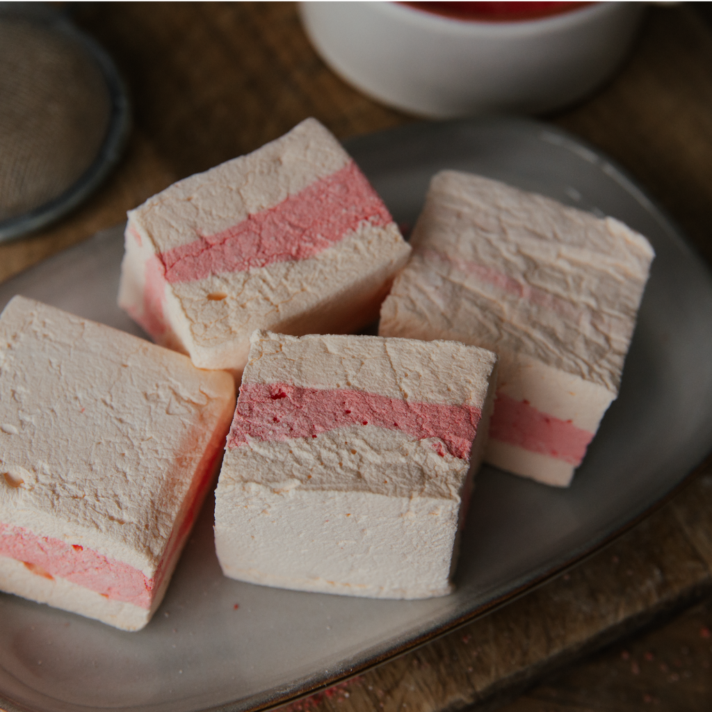 Layered marshmallows on a plate with a cup in the background