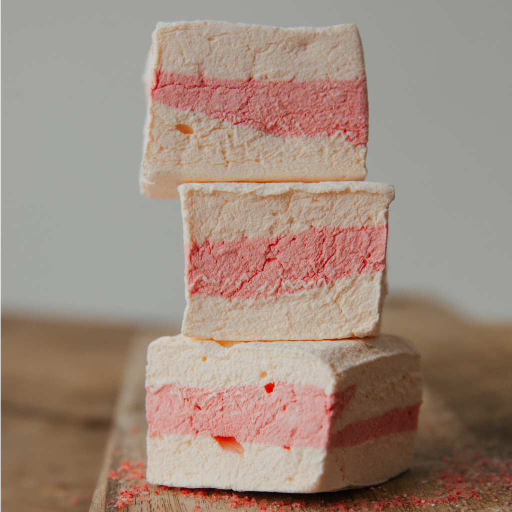 Stack of layered marshmallows with red and orange colors on a wooden surface.