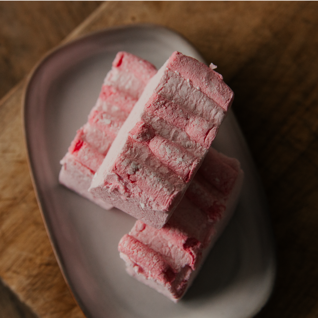 Pink candyfloss marshmallows on a plate with a wooden background