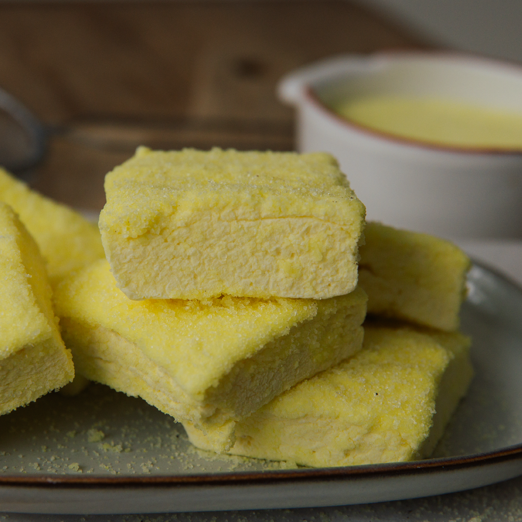 Yellow marshmallow slices on a plate with a bowl of yellow sherbet in the background.