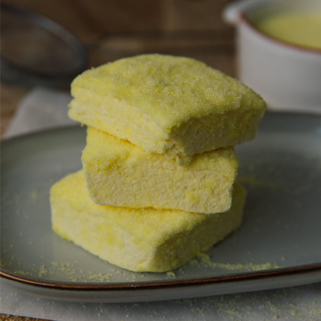 Three yellow marshmallow blocks stacked on a gray plate with a blurred background.